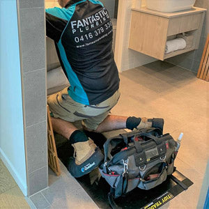 A plumber wearing cleanboots and working on a medium tidy tradie work mat.