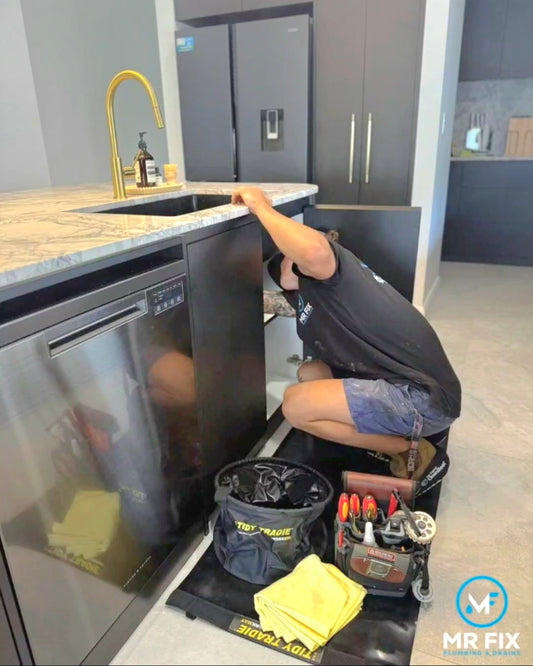 A plumber working on a medium Tidy Tradie Work Mat while wearing cleanboot covers and using a small Tidy Tradie work bin.