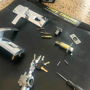 A locksmith placing greasy lock parts on a large tidy tradie work mat, keeping the floor clean.