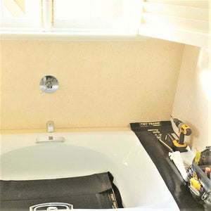 A carpenter protecting a bathtub by placing his tools on a rubber tidy tradie work mat.